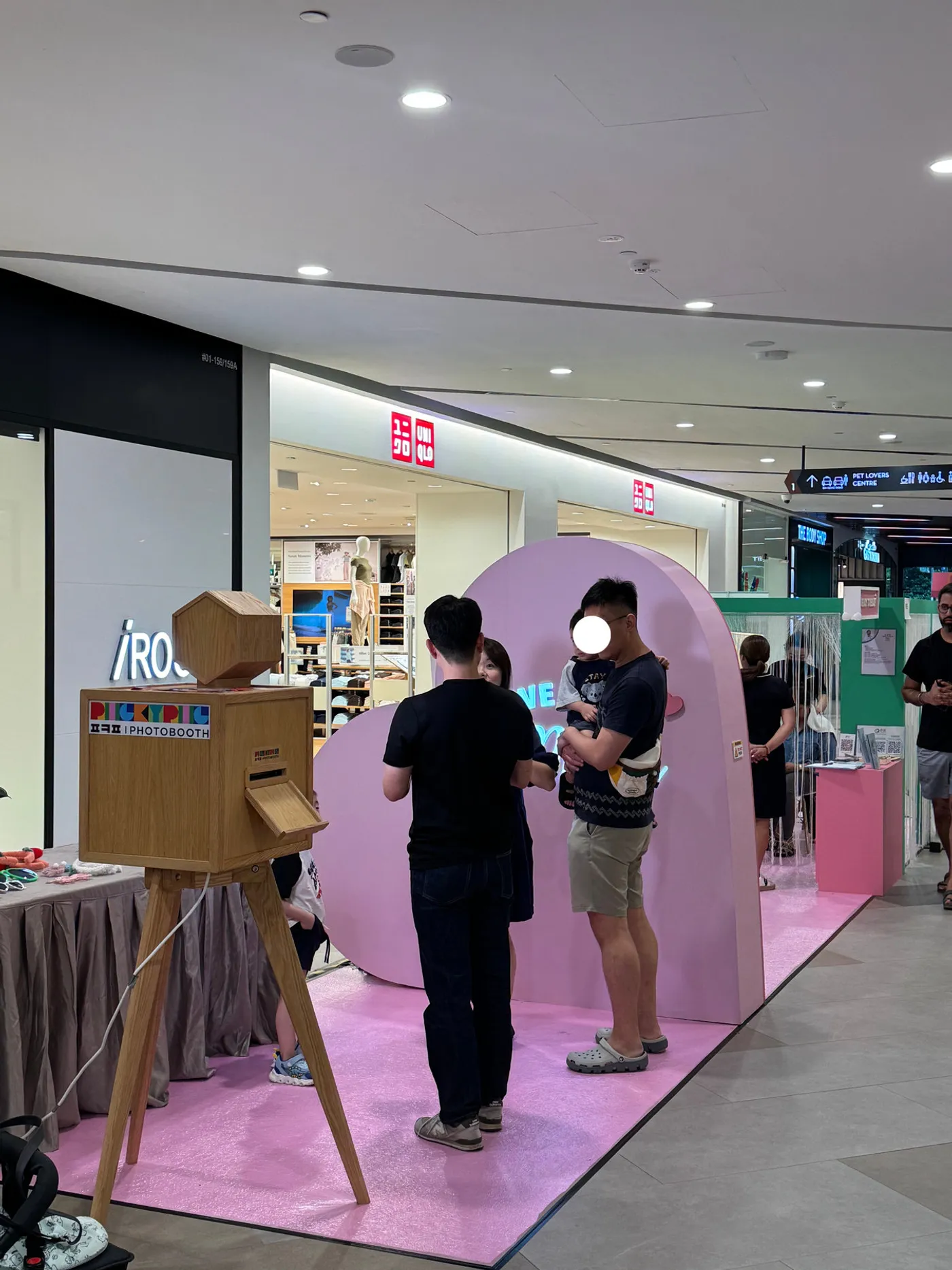 Shoppers at a pink photo zone beside a wooden PickyPic booth at Great World mall